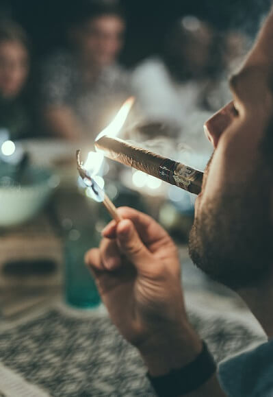 A patron sitting across the table from friends lighting a cigar in a bar lounge space while smoke emits.