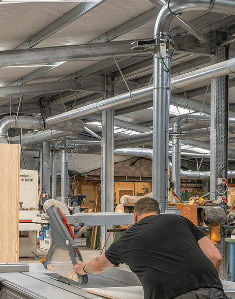 A woodworker operating machinery while working on a project in a large facility with Nordfab Ducting show installed and attached to equipment.