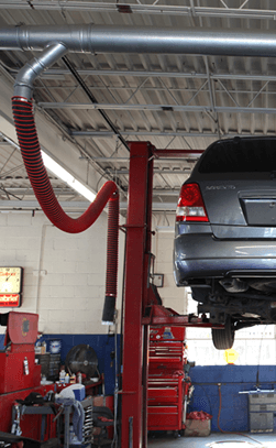 An SUV in car dealership shown lifted with overhead exhaust removal system installed.