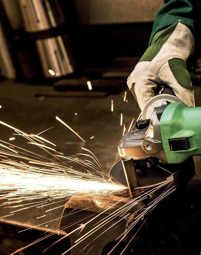 A machine operator working on a project using a grinder while sparks emit from the work piece.